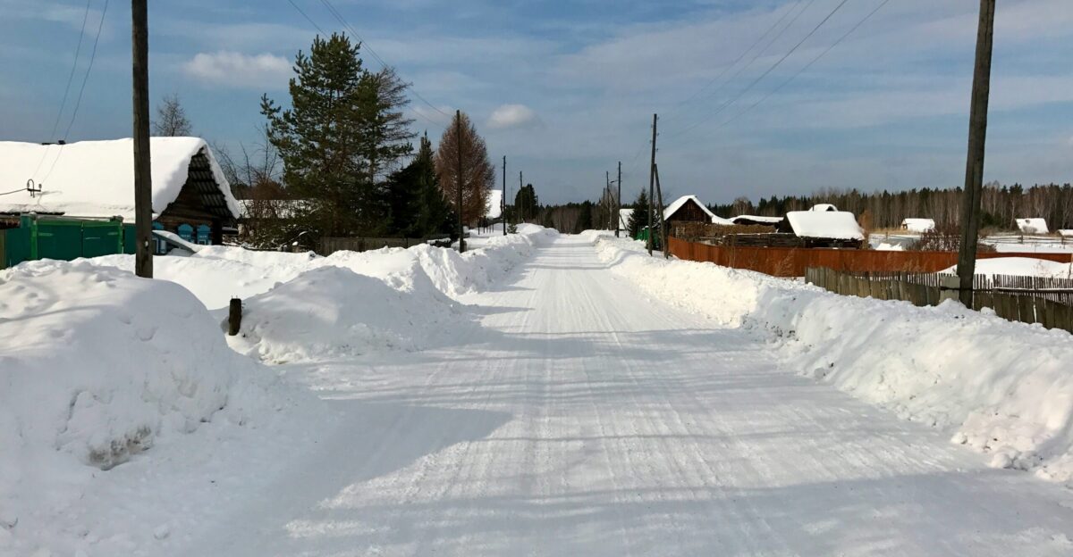 a road that is covered in snow with houses in the background