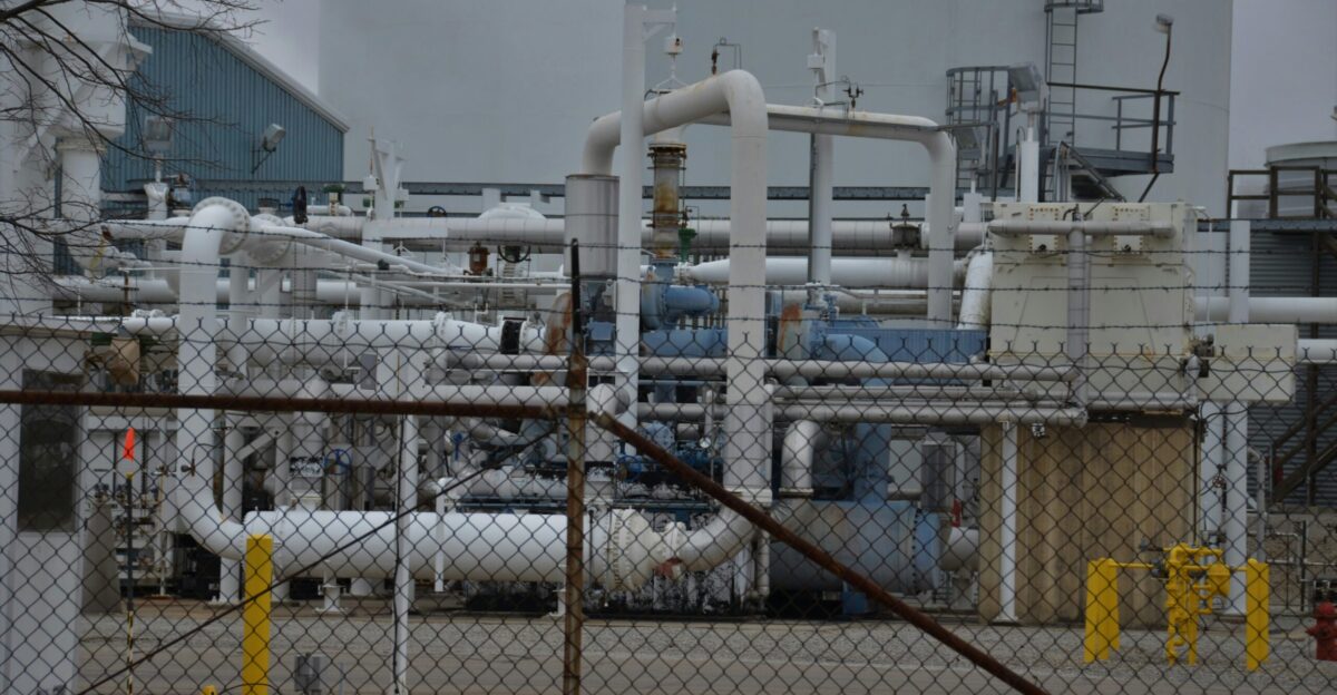 a factory with pipes and pipes behind a chain link fence