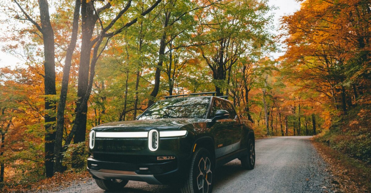 a black car parked on a road surrounded by trees