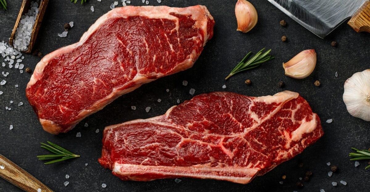 two steaks on a cutting board next to garlic garlic and a knife