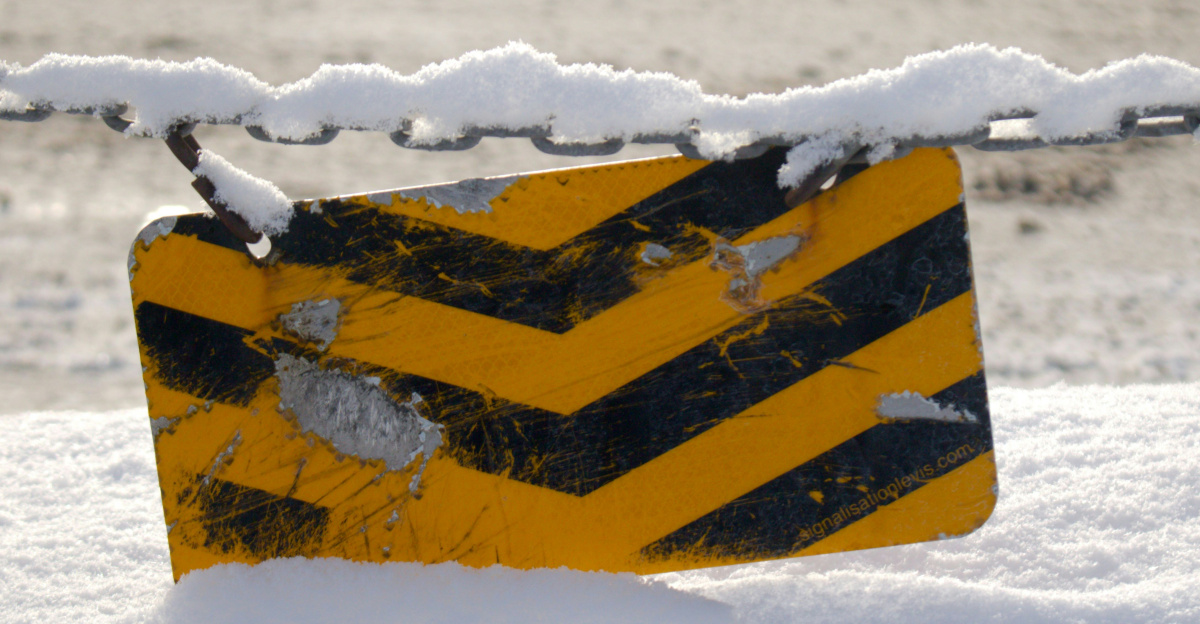 A yellow and black sign sitting on top of snow covered ground