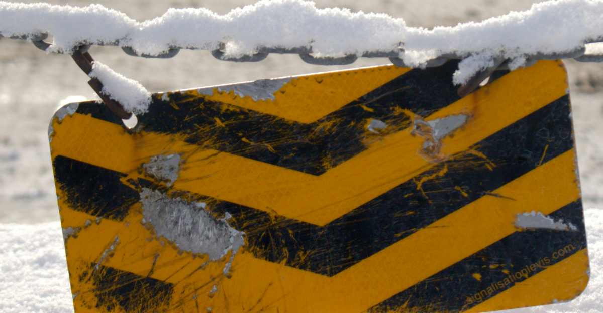 A yellow and black sign sitting on top of snow covered ground