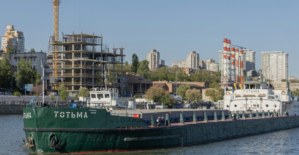 A cargo ship floats by buildings in a city