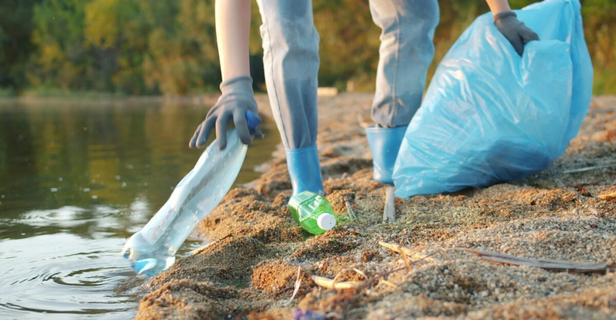 Person picking up plastic bottle near water