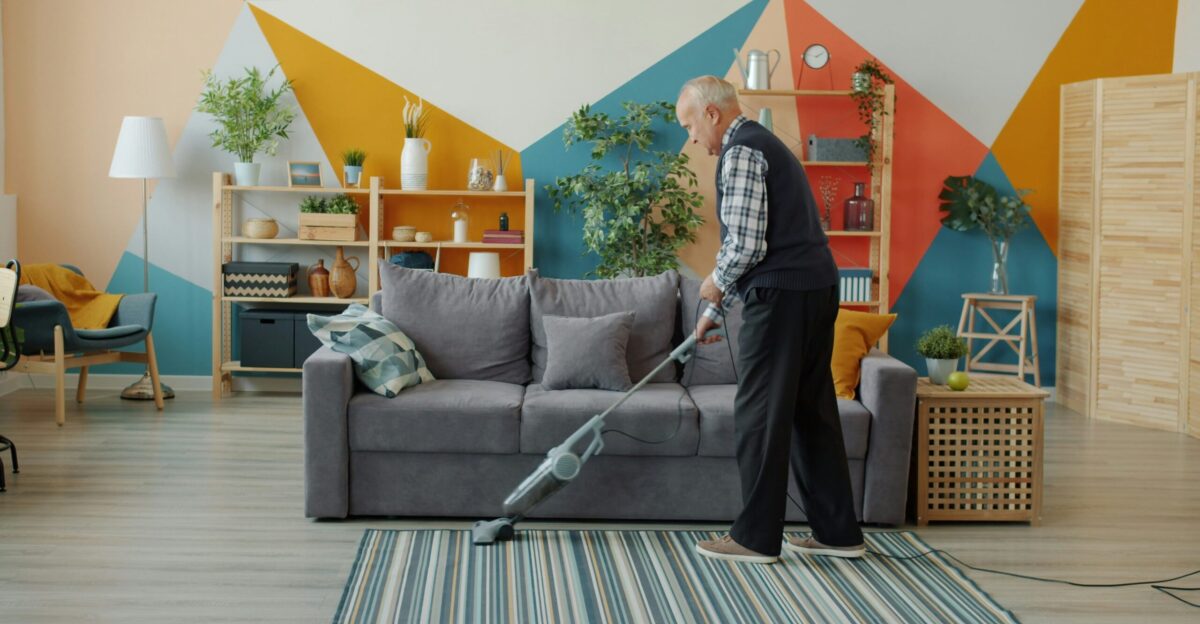 Elderly woman vacuuming a colorful living room floor