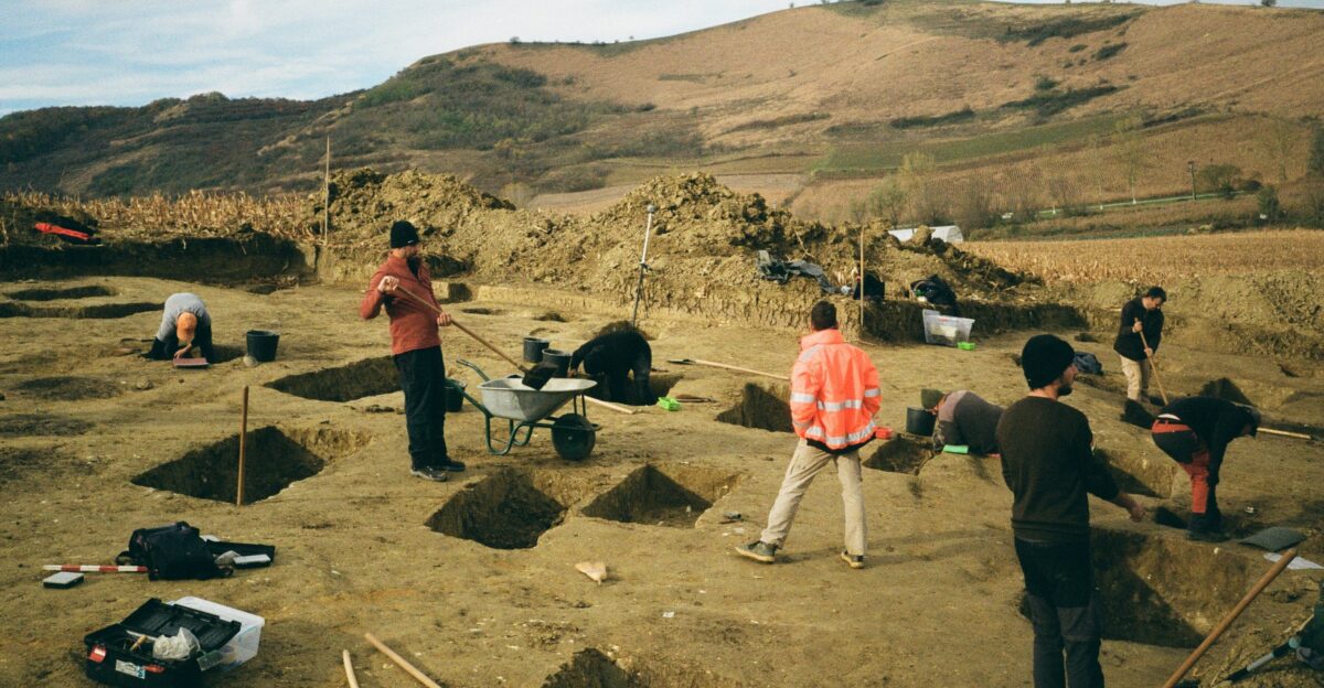 Archaeologists excavating a field with tools and trenches