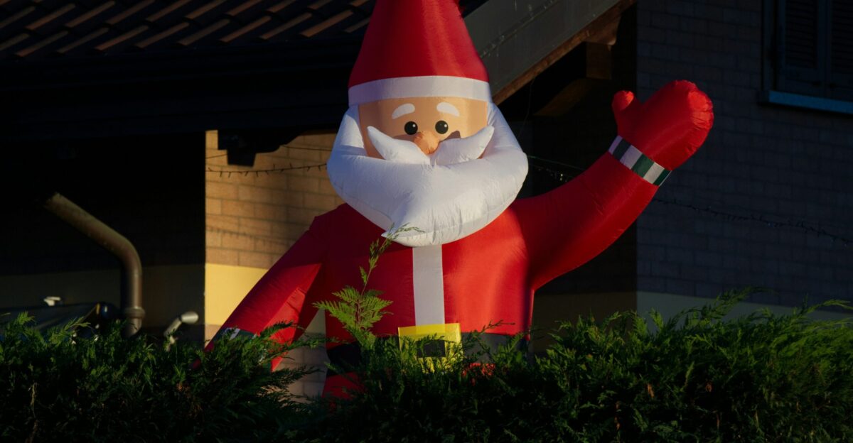 Inflatable santa claus decoration waves from behind hedge
