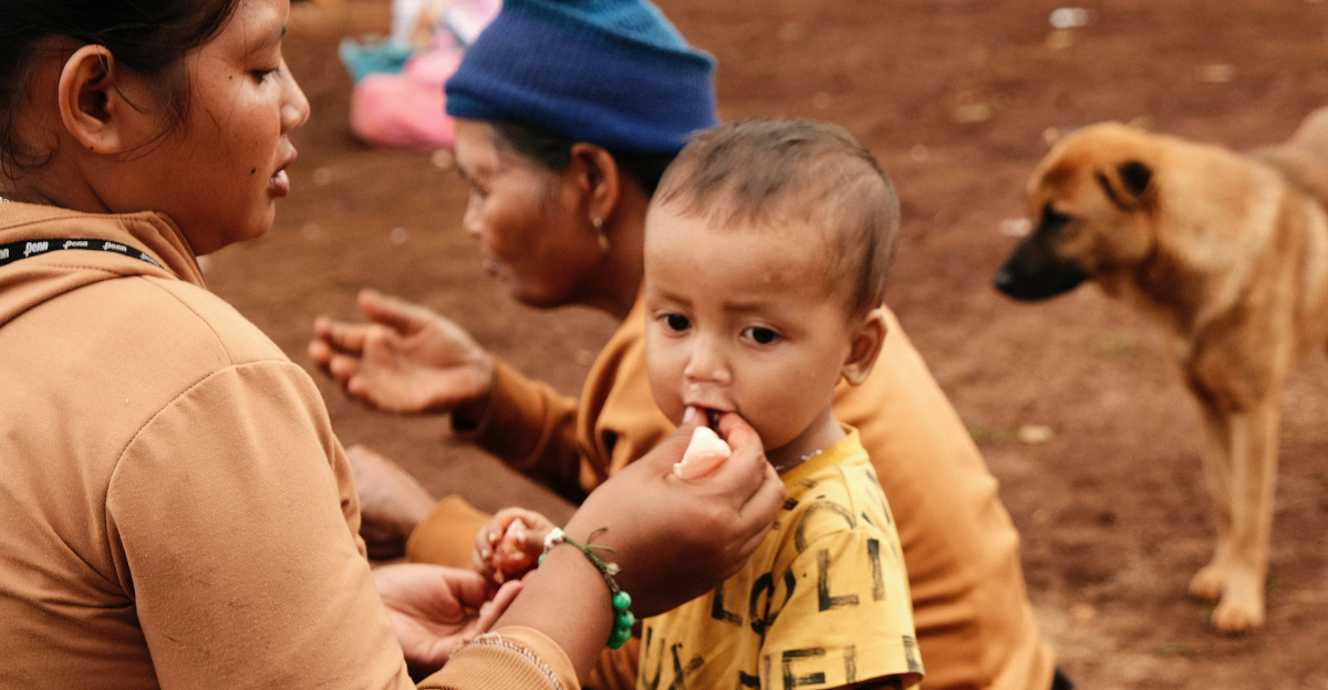 Woman feeding young child with a dog nearby