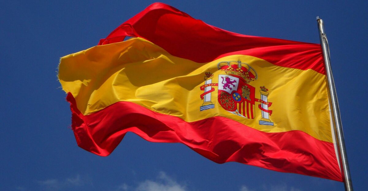 Vibrant Spanish flag waving against a clear blue sky and clouds