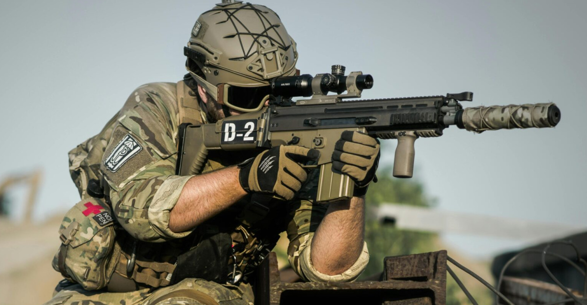 A soldier in full camouflage gear aiming a rifle while in a tactical stance outdoors.