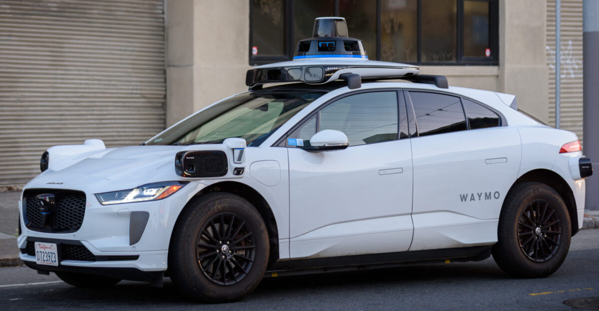 A front quarter view of a Jaguar I-Pace modified by Waymo for use as an autonomous vehicle stopped at a traffic light in San Francisco