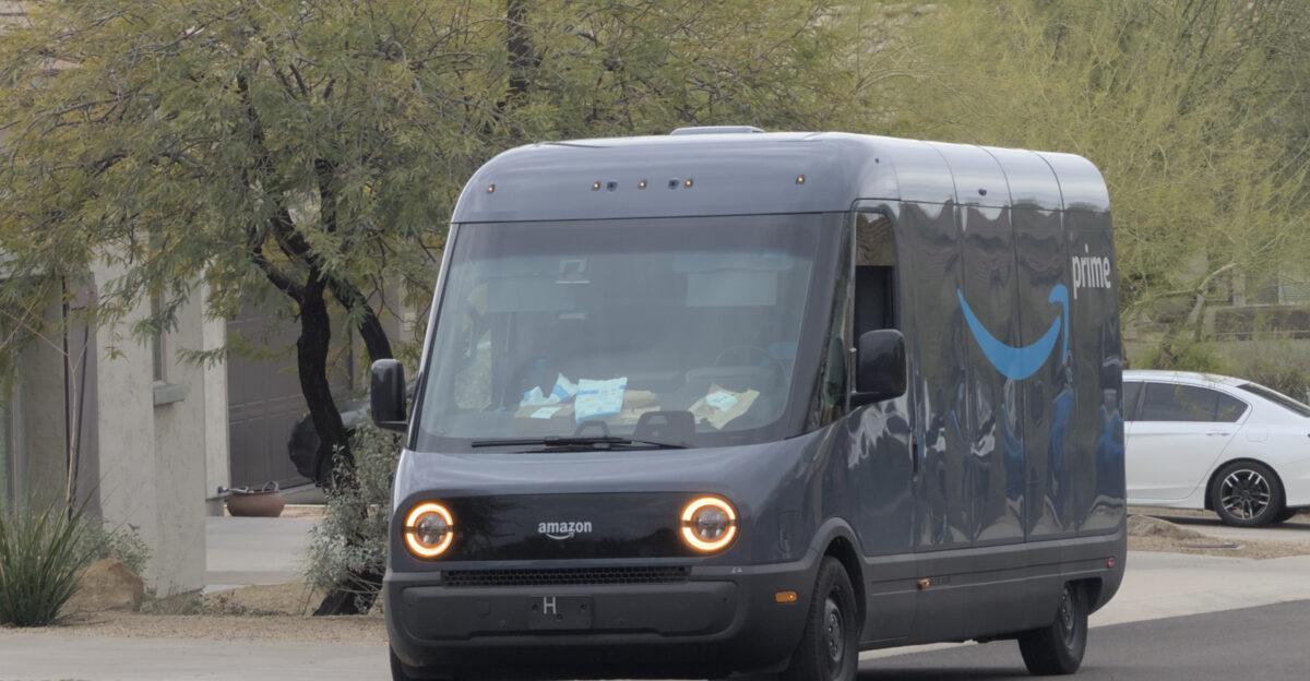 A glossy grey truck delivery van parked with it s hazard lights on It has a large blue amazon logo marked on the side It s incredibly clean Bags and cardboard boxes are piled up on the dashboard