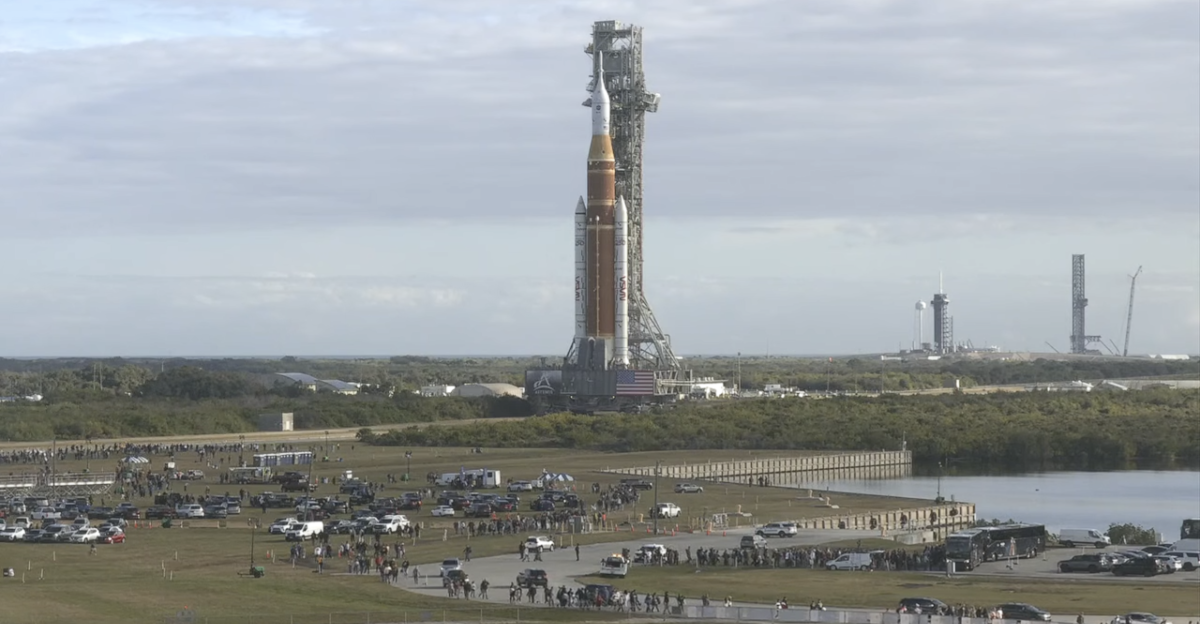 A view of the Artemis II s missions rocket being rolled out with cars in the foreground