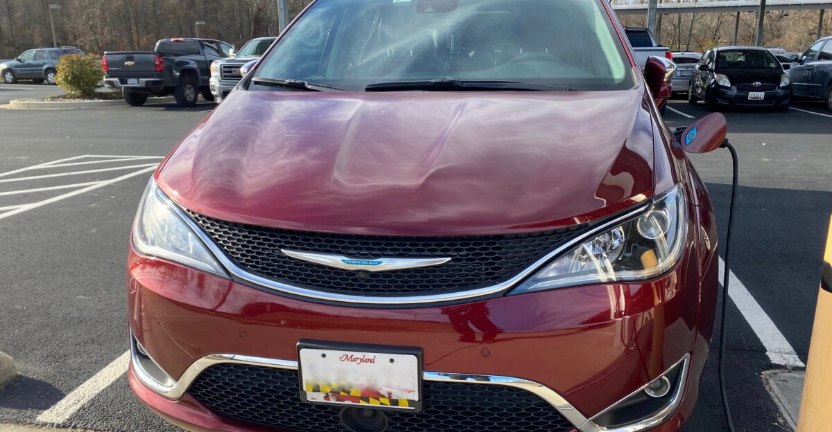 Chrysler Pacifica Hybrid minivan finished in Velvet Red pearl-coat Photographed while fueling at a charging station that is solar panel powered