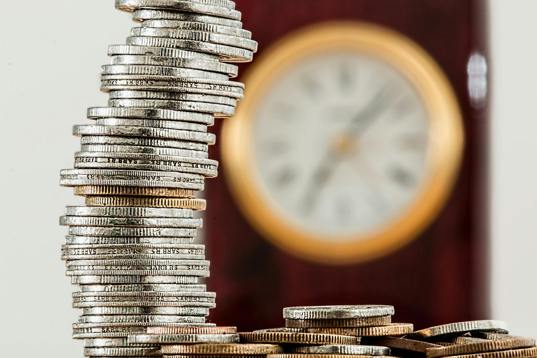A close-up image of stacked coins with a blurred clock symbolizing time and money relationship