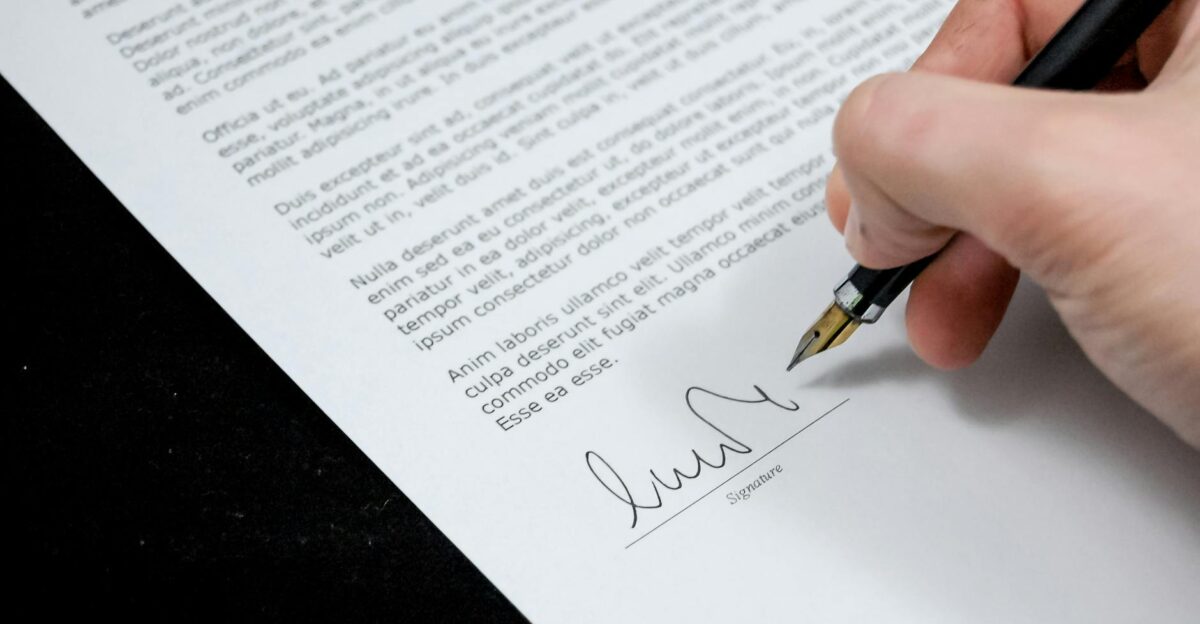 Close-up of a hand signing a formal document with a fountain pen indicating agreement