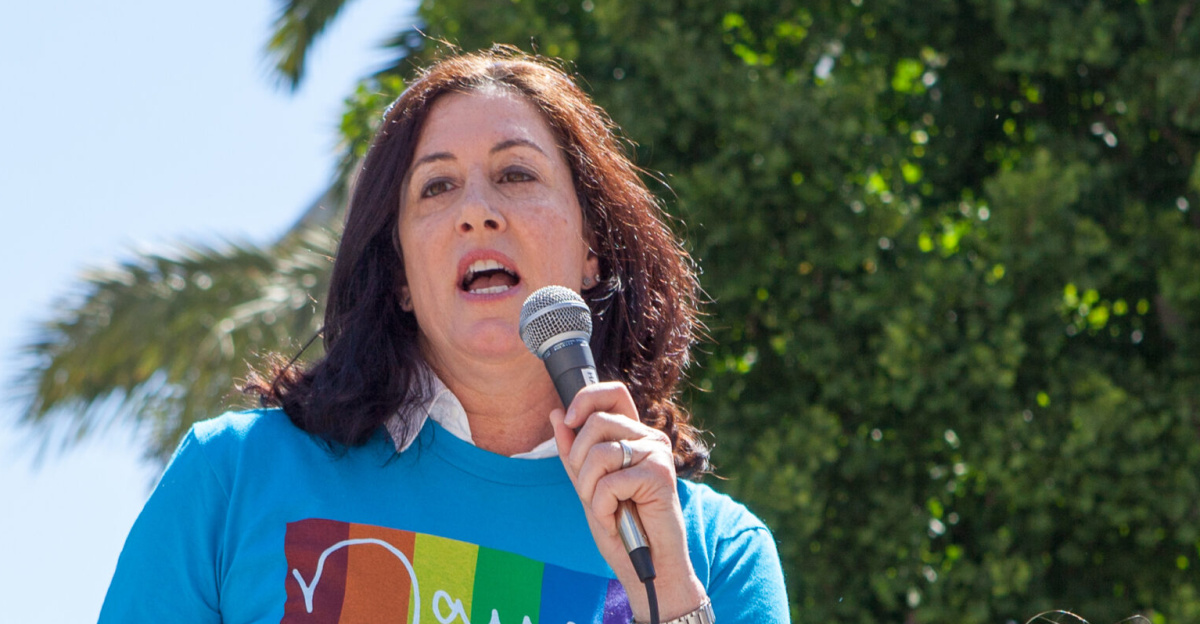 Christine Pelosi, standing alongisde her daughter and holding a sign reading "Families Belong Together", speaks at a "Families Belong Together" rally in San Francisco. Both mother and daughter wear T-shirts bearing the name of Christine's mother, representative Nancy Pelosi.