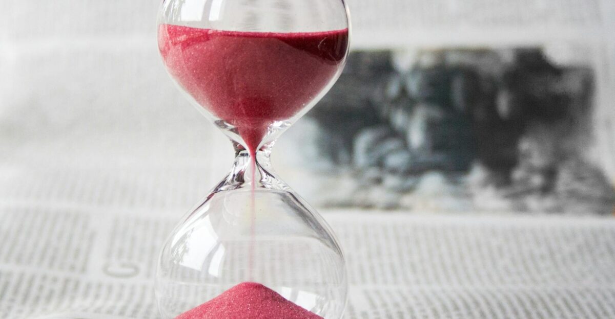 Close-up of a transparent hourglass with pink sand flowing placed on a newspaper background