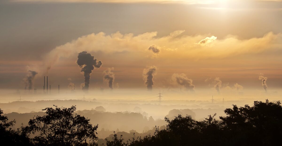 Smoke rising from factory chimneys at sunrise symbolizing pollution and environmental impact