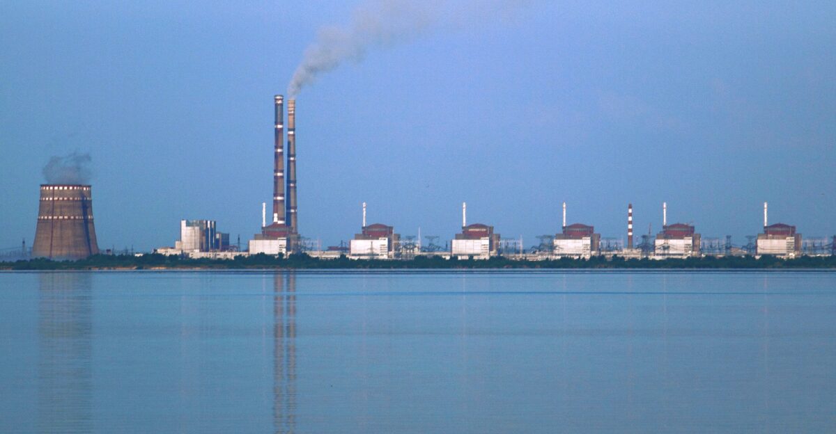 Two power stations at Enerhodar about 50 km from Zaporozhye in Ukraine viewed from across the Kakhovka Reservoir on the river Dnieper Photo taken from the Nikopol shore The nearer power station is Zaporizhzhia Nuclear Power Plant the biggest nuclear power station in Europe consisting of two cooling towers one largely obscured by the other at the left and 6 VVER reactor buildings The large building between the cooling towers and the reactors and the two tall smokestacks are at the Zaporizhzhia thermal power station about 3 km beyond the nuclear plant