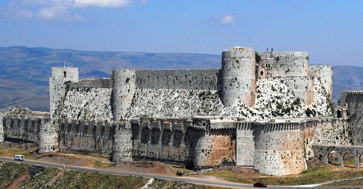 <p>Krak des Chevaliers is a Crusader castle in Syria and one of the most important preserved medieval castles in the world. The site was first inhabited in the 11th century by a settlement of Kurds; as a result it was known as Hisn al Akrad, meaning the "Castle of the Kurds". In 1142 it was given by Raymond II, Count of Tripoli, to the Knights Hospitaller. It remained in their possession until it fell in 1271. It became known as Crac de l'Ospital; the name Krak des Chevaliers was coined in the 19th century.
The Hospitallers began rebuilding the castle in the 1140s and were finished by 1170 when an earthquake damaged the castle. The order controlled a number of castles along the border of the County of Tripoli, a state founded after the First Crusade. Krak des Chevaliers was amongst the most important and acted as a centre of administration as well as a military base. After a second phase of building was undertaken in the 13th century, Krak des Chevaliers became a concentric castle. This phase created the outer wall and gave the castle its current appearance. The first half of the century has been described as Krak des Chevaliers' "golden age". At its peak, Krak des Chevaliers housed a garrison of around 2,000. Such a large garrison allowed the Hospitallers to extract tribute from a wide area. From the 1250s the fortunes of the Knights Hospitaller took a turn for the worse and in 1271 Krak des Chevaliers was captured by the Mamluk Sultan Baibars after a siege lasting 36 days.
Renewed interest in Crusader castles in the 19th century led to the investigation of Krak des Chevaliers, and architectural plans were drawn up. In the late 19th or early 20th century a settlement had been created within the castle, causing damage to its fabric. The 500 inhabitants were moved in 1933 and the castle was given over to the French state, under which a programme of clearing and restoration was carried out. When Syria declared independence in 1946, the castle left French control. Krak des Chevaliers is located approximately 40 kilometres (25 mi) west of the city of Homs, close to the border of Lebanon, and is administratively part of the Homs Governorate. Since 2006, the castles of Krak des Chevaliers and Qal'at Salah El-Din have been recognised by UNESCO as a World Heritage Site.
The modern Arabic name for the castle is Qalaat el Hosn, which translates as "stronghold castle"; this derives from the name of an earlier fortification on the site called Hisn el Akrad, meaning stronghold of the Kurds.It was called by the Franks Le Crat and then by a confusion with karak (fortress), Le Crac. Crat was probably the Frankish version of Akrad, the word for Kurds. After the Knights Hospitaller took control of the castle, it became known as Crac de l'Ospital; the name Crac des Chevaliers (alternatively spelt Krak des Chevaliers) was introduced by Guillaume Rey in the 19th century.
Location
The castle sits atop a 650-metre (2,130 ft) high hill east of Tartus, Syria, in the Homs Gap.[5] On the other side of the gap, 27 kilometres (17 mi) away, was the 12th-century Gibelacar Castle. The route through the strategically important Homs Gap connects the cities of Tripoli and Homs. To the north of the castle lies the Jebel Ansariyah, and to the south Lebanon. The surrounding area is fertile, benefiting from streams and abundant rainfall.
Compared to the Kingdom of Jerusalem, the other Crusader states had less land suitable for farming; however, the limestone peaks of Tripoli were well-suited to defensive sites.
Property in the County of Tripoli granted to the Knights Templar in the 1140s included the Castle of the Kurds, the towns of Rafanea and Montferrand, and the Buqai'ah plain separating Homs and Tripoli. Homs was never under Crusader control, so the region around the Castle of the Kurds was vulnerable to expeditions from the city. While its proximity caused the Knights problems with regard to defending their territory, it also meant it was close enough for them to raid. Because of its command of the plain, the castle became the Knights' most important base in the area.
History
The Levant in 1135 (left), with Crusader states marked by a red cross and the region in 1190 (right)
According to Arab documents, the site of the later castle was first occupied in 1030 by a group of Kurds; it was from this settlement that the site derived its name. When building castles, Muslims often chose high sites such as hills and mountains that provided natural obstacles. While journeying towards Jerusalem in January 1099, the company of Raymond IV of Toulouse came under attack. The garrison of al-Akrad harried Raymond's foragers.The following day he marched on the castle and found it deserted. The Franks briefly occupied the castle in February but abandoned when they continued their march towards Jerusalem. Permanent occupation began in 1110 when Tancred, Prince of Galilee took control of the site. The early castle was very different from the extant remains. No trace of this first castle on the site survives.
The origins of the Knights Hospitaller are unclear, but the order probably emerged around the 1070s in Jerusalem. It started as a religious order which cared for the sick, and later looked after pilgrims to the Holy Land. After the success of the First Crusade in capturing Jerusalem in 1099, many crusaders donated their new property in the Levant to the Hospital of St John. Early donations were in the newly formed Kingdom of Jerusalem, but over time the Order extended its holdings to the Crusader states of the County of Tripoli and the Principality of Antioch. Evidence suggests that in the 1130s the order was becoming militarised in 1136 Fulk, King of Jerusalem, granted the newly built castle at Bethgibelin to the order and a papal bull from between 1139 and 1143 may indicate the order was hiring people to defend pilgrims. There were other military orders, such as the Order of the Temple, which offered protection to pilgrims.
From Guillaume Rey Étude sur les monuments de l'architecture militaire des croisés en Syrie et dans l'île de Chypre (1871).
Between 1142 and 1144 Raymond II, Count of Tripoli, granted the order property in the County. According to historian Jonathan Riley-Smith, the Hospitallers effectively established a "palatinate" within Tripoli. The property included castles with which the Knights Templar were expected to defend Tripoli. Including Krak des Chevaliers, the Hospitallers were given five castles along the borders of the state. The order's agreement with Raymond II allowed them to dominate the area; if Raymond II did not accompany the Knights on campaign, the spoils belonged entirely to the order, and if he was present it was split equally between the count and the order. Raymond II also could not make peace with the Muslims without the permission of the Hospitallers. The Hospitallers made Krak des Chevaliers a centre of administration for their new property. The work they undertook at the castle would make it one of the most elaborate Crusader fortifications in the Levant.
After acquiring the site in 1142, they began building a new castle, replacing the Kurdish fortification. The work lasted until 1170, when an earthquake damaged the castle. An Arab source mentions the quake destroyed the castle's chapel. It was replaced with the present chapel. In 1163 the Crusaders were victorious over Nur ad-Din in the Battle of al-Buqaia near Krak des Chevaliers.
Drought conditions between 1175 and 1180 prompted the Crusaders to sign a two-year truce with the Muslims, but Tripoli was not included in the terms. During the 1180s raids by Christians and Muslims into each other's territory became more frequent. In 1180, Saladin ventured into the County of Tripoli, ravaging the area. Unwilling to meet him in open battle, the Crusaders retreated to the relative safety of their fortifications. Without capturing the castles, Saladin could not secure control of the area, and once he retreated the Hospitallers were able to revitalise their damaged lands. The Battle of Hattin in 1187 was a disastrous defeat for the Crusaders: Guy of Lusignan, King of Jerusalem, was captured, as was the True Cross, a relic discovered during the First Crusade. Afterwards Saladin ordered the execution of the captured Templar and Hospitaller knights, such was the importance of the two orders in defending the Crusader states. After the battle, the Hospitaller castles of Belmont, Belvoir, and Bethgibelin fell to Muslim armies. Following these losses, the Order focussed its attention on its castles in Tripoli. In May 1188 Saladin led an army to attack Krak des Chevaliers, but on seeing the castle decided it was too well defended and marched on the Hospitaller castle of Margat, which he also failed to capture.
Another earthquake struck in 1202, and it may have been after this event that the castle was remodelled. The 13th-century work was the last period of building at Krak des Chevaliers and gave it its current appearance. An enclosing stone circuit was built between 1142 and 1170; the earlier structure became the castle's inner court or ward. If there was a circuit of walls surrounding the inner court that pre-dated the current outer walls, no trace of it has been discovered.
The first half of the 13th century has been characterised as Krak des Chevaliers' "golden age". While other Crusader strongholds were under threat, Krak des Chevaliers and its garrison of 2,000 soldiers dominated the surrounding area. It was effectively the centre of a principality which remained in Crusader hands until 1271 and was the only major inland area to remain constantly under Crusader control in this period. Crusaders passing through the area would often stop at the castle, and probably made donations. King Andrew II of Hungary visited in 1218 and proclaimed the castle was the "key of the Christian lands". He was so impressed with the castle he gave a yearly income of 60 marks to the Master and 40 to the brothers. Geoffroy de Joinville, uncle of the famous chronicler of the Crusades Jean de Joinville, died at Krak des Chevaliers in 1203 or 1204 and was buried within the castle's chapel.
The main contemporary sources relating to Krak des Chevaliers were written by Muslims. They tend to emphasise Muslim success and overlook setbacks against the Crusaders, but they suggest that the Knights Hospitaller forced the settlements of Hama and Homs to pay tribute to the order. This situation lasted as long as Saladin's successors warred between themselves. The proximity of Krak des Chevaliers to Muslim territories allowed it to take on an offensive role, acting as a base from which neighbouring areas could be attacked. By 1203 the garrison were making raids on Montferrand (which was under Muslim control) and Hama, and in 1207 and 1208 the castle's soldiers took part in an attack on Homs. Krak des Chevaliers acted as a base for expeditions to Hama in 1230 and 1233 after the amir refused to pay tribute. The former was unsuccessful, but the 1233 expedition was a show of force that demonstrated the importance of Krak des Chevaliers.
In the 1250s, the fortunes of the Hospitallers at Krak des Chevaliers took a turn for the worse. An army estimated to number 10,000 men ravaged the country around the castle in 1252. After this, it seems the order's finances were badly affected. In 1268 Master Hugh Revel complained that the area, which had previously been home to around 10,000 people, was deserted and the order's property in the Kingdom of Jerusalem was producing little income; he also noted that by this point there were only 300 of the order's brothers left in the east. On the Muslim side, a new Sultan, Baibars, seized power in 1260 and united Egypt and Syria. One of the effects was that Muslim settlements which had previously paid tribute to the Hospitallers at Krak des Chevaliers were no longer intimidated into doing so.
Baibars ventured in the area around Krak des Chevaliers in 1270 and allowed his men to graze their animals on the fields around the castle. When he received news that year that King Louis IX of France was leading the Eighth Crusade, Baibars left for Cairo. Louis died in 1271 and Baibars returned north to deal with Krak des Chevaliers. Before marching on the castle he captured the smaller castles in the area, including Chastel Blanc. On 3 March, Baibars' army arrived at Krak des Chevaliers. By the time the Sultan arrived the castle may already have been blockaded by Mamluk forces for several days. There are three Arabic accounts of the siege; only one, that of Ibn Shaddad, was by a contemporary although he was not present. Peasants who lived in the area had fled to the castle for safety and were kept in the outer ward. As soon as Baibars arrived he began erecting mangonels, powerful siege weapons which he would turn on the castle. According to Ibn Shaddad, two days later the first line of defences was captured by the besiegers; he was probably referring to a walled suburb outside the castle's entrance.
Rain interrupted the siege, but on 21 March a triangular outwork immediately south of Krak des Chevaliers, possibly defended by a timber palisade, was captured. On 29 March, the tower in the south-west corner was undermined and collapsed. Baibars' army attacked through the breach and on entering the outer ward where they encountered the peasants who had sought refuge in the castle. Though the outer ward had fallen, and in the process a handful of the garrison killed, the Crusaders retreated to the more formidable inner ward. After a lull of ten days, the besiegers conveyed a letter to the garrison, supposedly from the Grand Master of the Knights Hospitaller in Tripoli which granted permission for them to surrender. Although the letter was a forgery, the garrison capitulated and the Sultan spared their lives. The new owners of the castle undertook repairs, focussed mainly on the outer ward. The Hospitaller chapel was converted to a mosque and two mihrabs were added to the interior.
Later history
After the Franks were driven from the Holy Land in 1291, European familiarity with the castles of the Crusades declined. It was not until the 19th century that interest in these buildings was renewed, so there are no detailed plans from before 1837. Guillaume Rey was the first to scientifically study Crusader castles in the Holy Land. In 1871 he published the work Etudes sur les monuments de l'architecture militaire des Croisés en Syrie et dans l'ile de Chypre; it included plans and drawings of the major Crusader castles in Syria, including Krak des Chevaliers. In some instances his drawings were inaccurate, however for Krak des Chavaliers they record features which have since been lost.
Paul Deschamps visited the castle in February 1927. Since Rey had visited in the 19th century a village of 500 people had been established within the castle. Renewed inhabitation had damaged the site: underground vaults had been used as rubbish tips and in some places the battlements had been destroyed. Deschamps and fellow architect François Anus attempted to clear some of the detritus; General Maurice Gamelin assigned 60 Alawite soldiers to help. Deschamps left in March 1927, and work resumed when he returned two years later. The culmination of Deschamp's work at the castle was the publication of Les Châteaux des Croisés en Terre Sainte I: le Crac des Chevaliers in 1934, with detailed plans by Anus.[36] The survey has been widely praised, described as "brilliant and exhaustive" by military historian D. J. Cathcart King in 1949[2] and "perhaps the finest account of the archaeology and history of a single medieval castle ever written" by historian Hugh Kennedy in 1994.
As early as 1929 there were suggestions that the castle should be taken under French control. On 16 November 1933 Krak des Chevaliers was given into the control of the French state, and cared for by the Académie des Beaux-Arts. The villagers were moved and paid F1 million between them in compensation. Over the following two years a programme of cleaning and restoration was carried out by a force of 120 workers. Once finished, Krak des Chevaliers was one of the key tourist attractions in the French Levant. Pierre Coupel, who had undertaken similar work at the Tower of the Lions and the two castles at Sidon, supervised the work. Despite the restoration, no archaeological excavations were carried out. The French Mandate of Syria and Lebanon, which had been established in 1920, ended in 1946 with the declaration of Syrian independence. The castle was made a World Heritage Site by UNESCO, along with Qal’at Salah El-Din, in 2006,[1] and is owned by the Syrian government. During the Syrian uprising which began in 2011 UNESCO voiced concerns that the conflict might lead to the damage of important cultural sites such as Krak des Chevaliers. It has been reported that the castle has been shelled by the Syrian army, and that the Crusader chapel has been damaged.
Architecture
Writing in the early 20th century, T. E. Lawrence, popularly known as Lawrence of Arabia, remarked that Krak des Chevaliers was perhaps the best preserved and most wholly admirable castle in the world, [a castle which] forms a fitting commentary on any account of the Crusading buildings of Syria. Castles in Europe provided lordly accommodation for their owners and were centres of administration; in the Levant the need for defence was paramount and was reflected in castle design. Kennedy suggests that The castle scientifically designed as a fighting machine surely reached its apogee in great buildings like Margat and Crac des Chevaliers.
Krak des Chevaliers can be classified both as a spur castle, due to its site, and after the 13th-century expansion a fully developed concentric castle. It was similar in size and layout to Vadum Jacob, a Crusader castle built in the late 1170s. Margat has also been cited as Krak des Chevaliers' sister castle. The main building material at Krak des Chevaliers was limestone; the ashlar facing is so fine that the mortar is barely noticeable. Outside the castle's entrance was a "walled suburb" known as a burgus, although no trace of it remains. To the south of the outer ward was a triangular outwork and the Crusaders may have intended to build stone walls and towers around it. It is unknown how it was defended at the time of the 1271 siege, though it has been suggested it was surrounded by a timber palisade. South of the castle the spur on which it stands is connected to the next hill, so that siege engines can approach on level ground. The inner defences are strongest at this point, with a cluster of towers connected by a thick wall.
Between 1142 and 1170 the Knights Hospitaller undertook a building programme on the site. The castle was defended by a stone curtain wall studded with square towers which projected slightly. The main entrance was between two towers on the eastern side, and there was a postern gate in the north-west tower. At the centre was a courtyard surrounded by vaulted chambers. The lay of the land dictated the castle's irregular shape. A site with natural defences was a typical location for Crusader castles and steep slopes provided Krak des Chevaliers with defences on all sides bar one, where the castle's defences were concentrated. This phase of building was incorporated into the later castle's construction.
When Krak des Chevaliers was remodelled in the 13th century, new walls surrounding the inner court were built. They followed the earlier walls, with a narrow gap between them in the west and south which was turned into a gallery from which defenders could unleash missiles. In this area, the walls were supported by a steeply sloping glacis which provided additional protection against both siege weapons and earthquakes. Four large, round towers project vertically from the glacis; they were used as accommodation for the Knights of the garrison, about 60 at its peak. The south-west tower was designed to house the rooms of the Grand Master of the Knights Hospitaller. Though the defences which once crested the walls of the inner wards no longer survive in most places, it seems that they did not extend for the entire circuit. Machicolations were absent from the southern face. The area between the inner court and the outer walls was narrow and not used for accommodation. In the east, where the defences were weakest, there was an open cistern filled by an aqueduct. It acted both as a moat and water supply for the castle.
At the north end of the small courtyard is a chapel and at the southern end is an esplanade. The esplanade is raised above the rest of the courtyard; the vaulted area beneath it would have provided storage and could have acted as stabling and shelter from missiles. Lining the west of the courtyard is the hall of the Knights. Though probably first built in the 12th century, the interior dates from the 13th-century remodelling. The tracery and delicate decoration is a sophisticated example of Gothic architecture, probably dating from the 1230s.
Chapel
The current chapel was probably built to replace the one destroyed by an earthquake in 1170. Only the east end of the original chapel, which housed the apse, and a small part of the south wall survive from the original chapel. The later chapel had a barrel vault and an uncomplicated apse; its design would have been considered outmoded by contemporary standards in France, but bears similarities to that built around 1186 at Margat. It was divided into three roughly equal bays. A cornice runs round the chapel at the point where the vault ends and the wall begins. Oriented roughly east to west, it was 21.5 metres (71 ft) long and 8.5 metres (28 ft) wide with the main entrance from the west and a second smaller one in the north wall. When the castle was remodelled in the early 13th century, the entrance was moved to the south wall. The chapel was lit by windows above the cornice, one at the west end, one on either side of the east bay, and one on the south side of the central bay, and the apse at the east end had a large window. In 1935 a second chapel was discovered outside the castle's main entrance, however it no longer survives.
Outer ward
The second phase of building work undertaken by the Hospitallers began in the early 13th century and lasted decades. The outer walls were built in the last major construction on the site, lending the Krak des Chevaliers its current appearance. Standing 9 metres (30 ft) high, the outer circuit had towers that projected strongly from the wall. While the towers of the inner court had a square plan and did not project far beyond the wall, the towers of the 13th-century outer walls were rounded. This design was new and even contemporary Templar castles did not have rounded towers. The technique was developed at Château Gaillard in France by Richard the Lionheart between 1196 and 1198. The extension to the south-east is of lesser quality than the rest of the circuit and was built at an unknown date. Probably around the 1250s a postern was added to the north wall.
Arrow slits in the walls and towers were distributed to minimise the amount of dead ground around the castle. Machicolations crowned the walls, offering defenders a way to hurl projectiles towards enemies at the foot of the wall. They were so cramped archers would have had to crouch inside them. The box machicolations were unusual: those at Krak des Chevaliers were more complex that those at Saône or Margat and there were no comparable features amongst Crusader castles. However, they bore similarities to Muslim work, such as the contemporary defences at the Citadel of Aleppo. It is unclear which side imitated the other, as the date they were added to Krak des Chevaliers is unknown, but it does provide evidence for the diffusion of military ideas between the Muslim and Christian armies. These defences were accessed by a wall-walk known as a chemin de ronde. In the opinion of historian Hugh Kennedy the defences of the outer wall were "the most elaborate and developed anywhere in the Latin east ... the whole structure is a brilliantly designed and superbly built fighting machine.
When the outer walls were built in the 13th century the main entrance was enhanced. A vaulted corridor led uphill from the outer gate in the north-east. The corridor made a hairpin turn halfway along its length, making it an example of a bent entrance. Bent entrances were a Byzantine innovation, but that at Krak des Chevaliers was a particularly complex example. It extended for 137 metres (450 ft), and along its length were murder-holes which allowed defenders to shower attackers with missiles. Anyone going straight ahead rather following the hairpin turn would emerge in the area between the castle's two circuits of walls. To access the inner ward, the passage had to be followed round.
Frescoes
</p>
Despite its predominantly military character, the castle is one of the few sites where Crusader art (in the form of frescoes) has been preserved. In 1935, 1955, and 1978 medieval frescoes were discovered within Krak des Chevaliers after later plaster and white-wash had decayed. They were painted on the interior and exterior of the main chapel, the chapel outside the main entrance which no longer survives. Writing in 1982, historian Jaroslav Folda noted that at the time there had been little investigation of Crusader frescoes which would provide a comparison for the fragmentary remains found at Krak des Chevaliers. Those in the chapel were painted on the masonry from the 1170–1202 rebuild. Mould, smoke, and moisture have made it difficult to preserve the frescoes. The fragmentary nature of the red and blue frescoes inside the chapel means they are difficult to assess. The one on the exterior of the chapel depicted the Presentation of Jesus at the Temple.