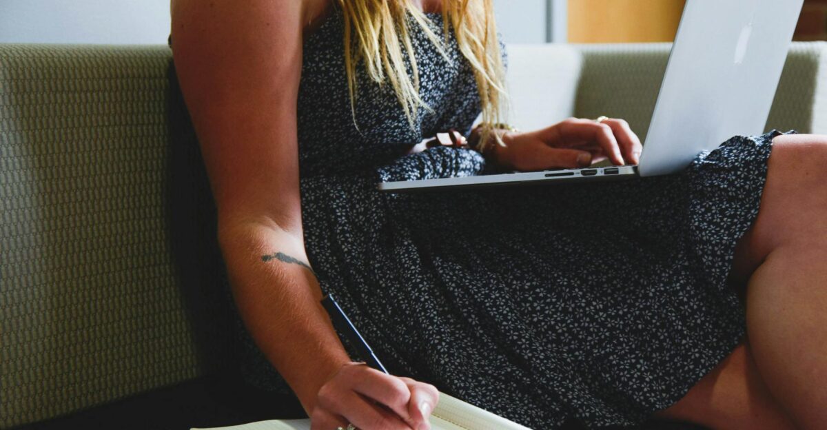 A woman multitasking with a laptop and writing notes highlighting remote work and study