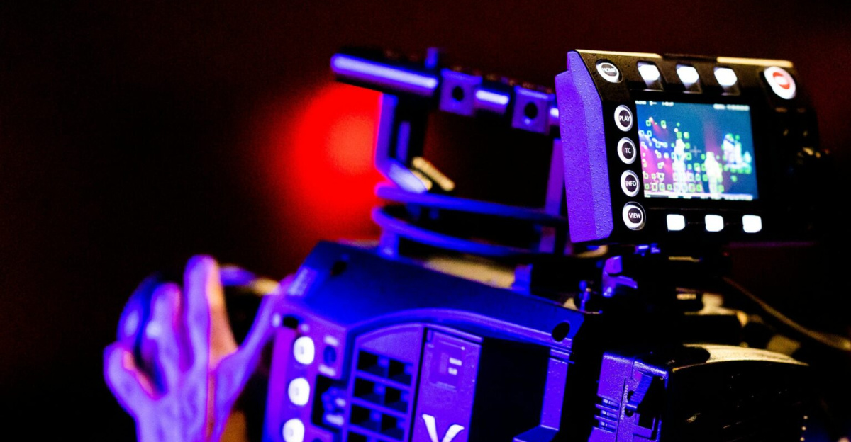Camera operator working with professional equipment in a dimly lit TV studio setting.