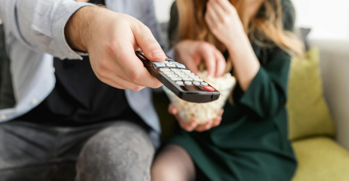 A couple enjoying a relaxing movie night sitting on a sofa with popcorn and a TV remote