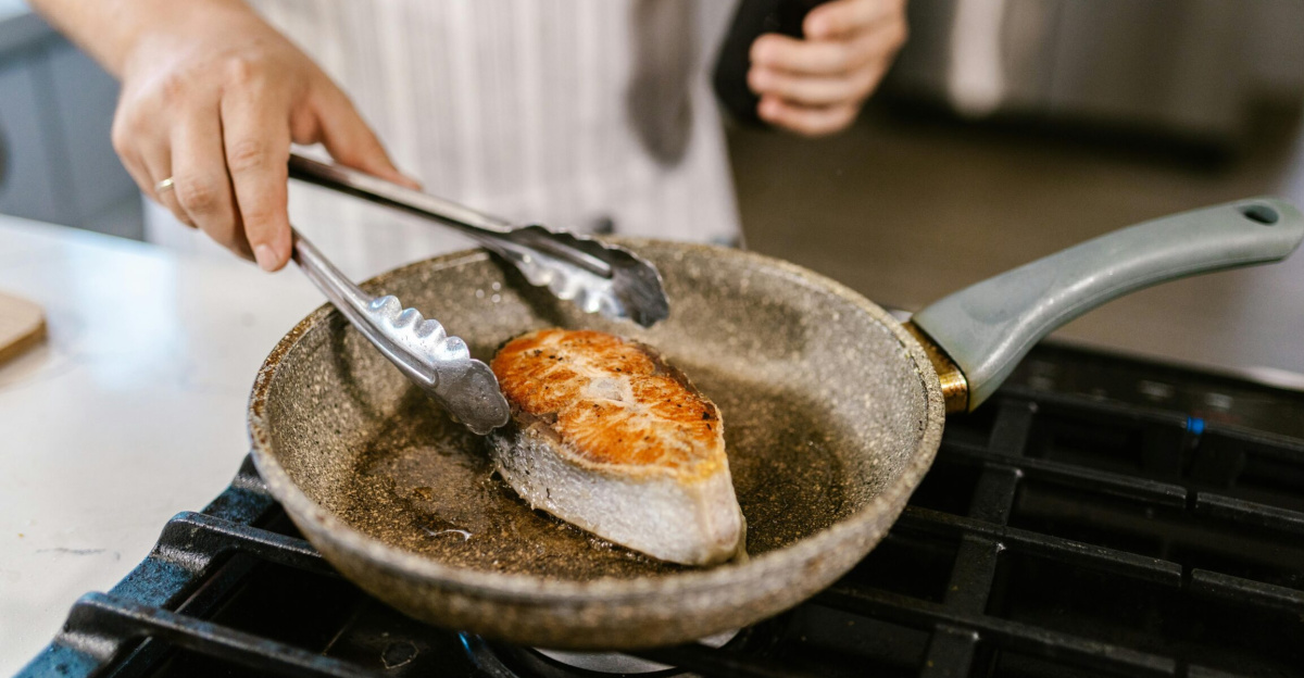 A close-up shot of a salmon steak being grilled in a non-stick pan in a kitchen setting. Perfect for cooking enthusiasts.