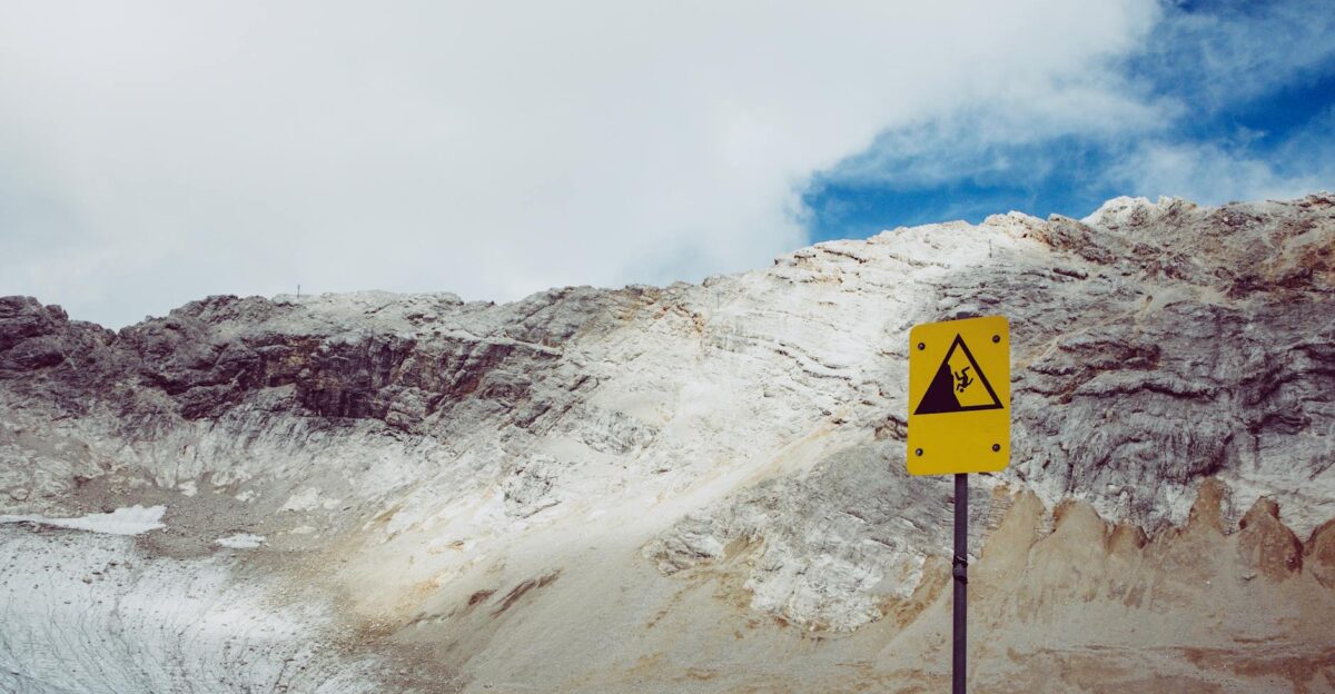 Mountainous terrain with a caution sign against falling rocks under a cloudy sky