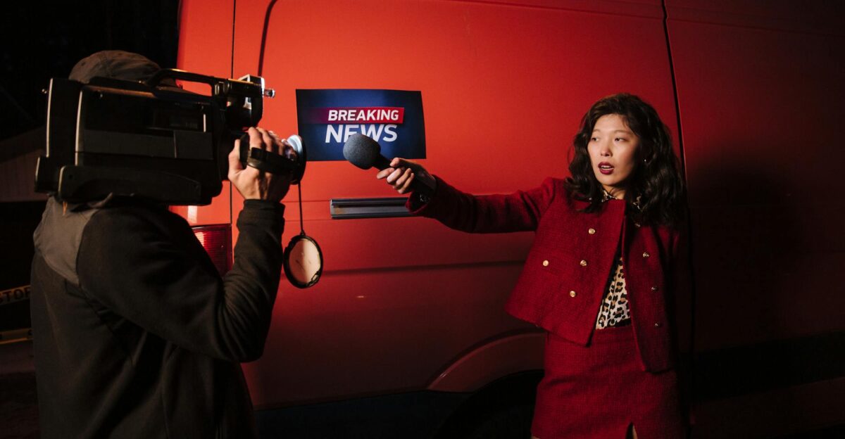 Asian female reporter with cameraman conducting a nighttime news broadcast beside a news van