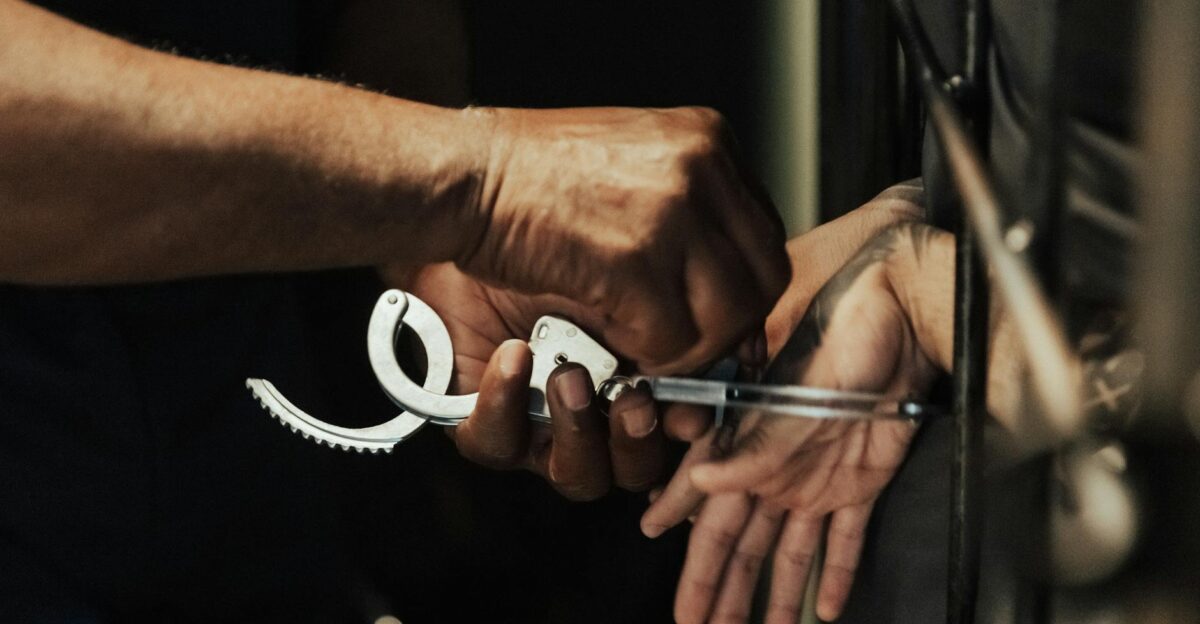 Close-up view of a person being handcuffed in a jail setting focusing on hands and handcuffs