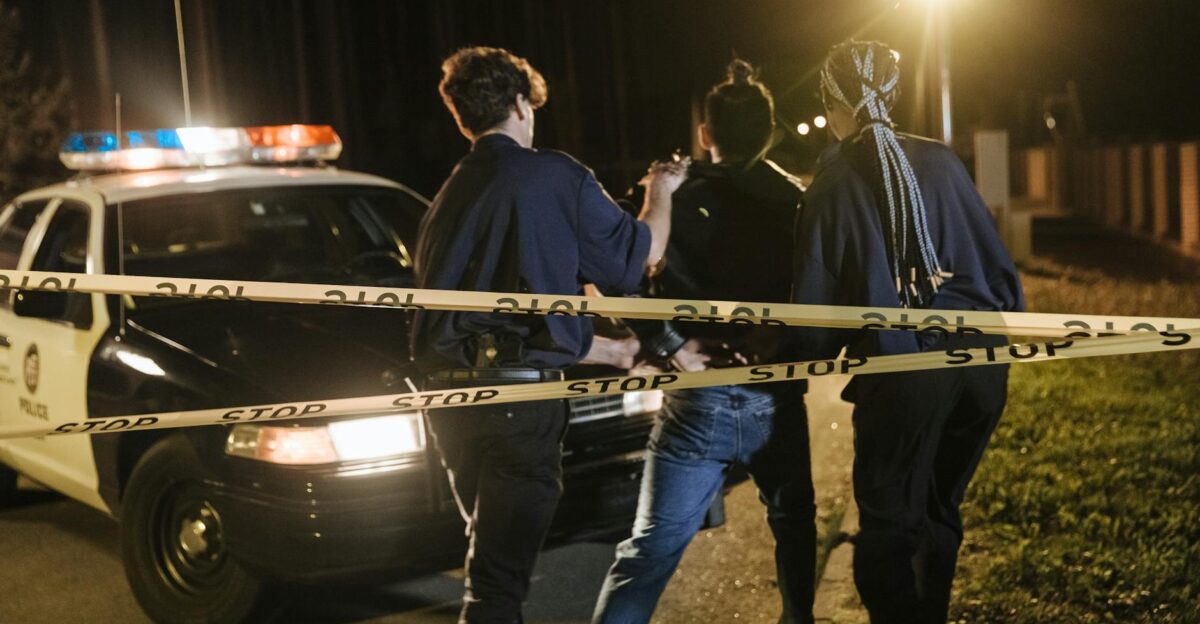 Nighttime arrest scene with police officers and patrol car behind caution tape