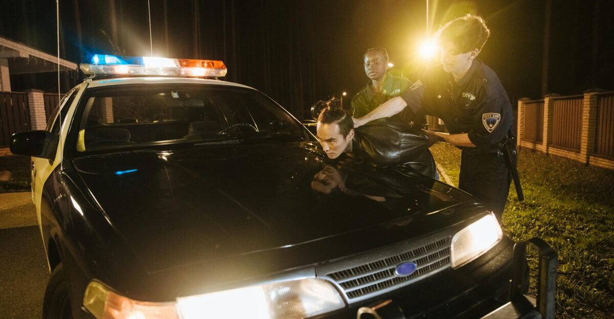 Police officers apprehending a suspect at night under streetlights by a patrol car