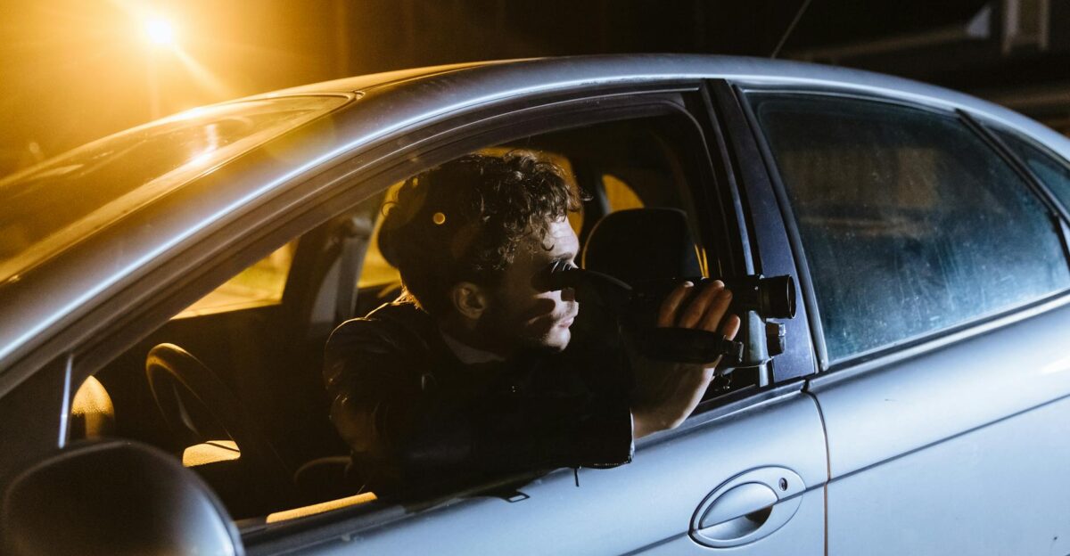 A man inside a car films outside through the window at night capturing a street scene