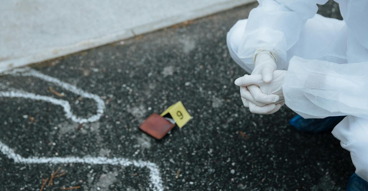 Forensic investigator examines crime scene outline on asphalt in protective suit