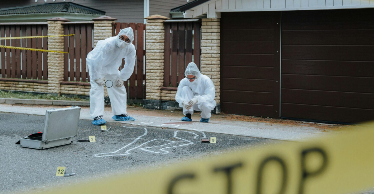 Forensic team examining crime scene with chalk outline and evidence markers outdoors.