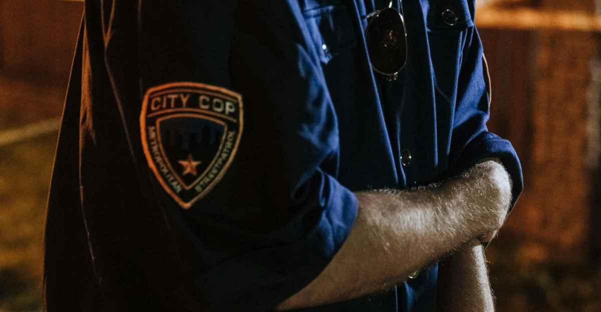 Police officer holding a gun with handcuffs hanging on belt in an outdoor setting.