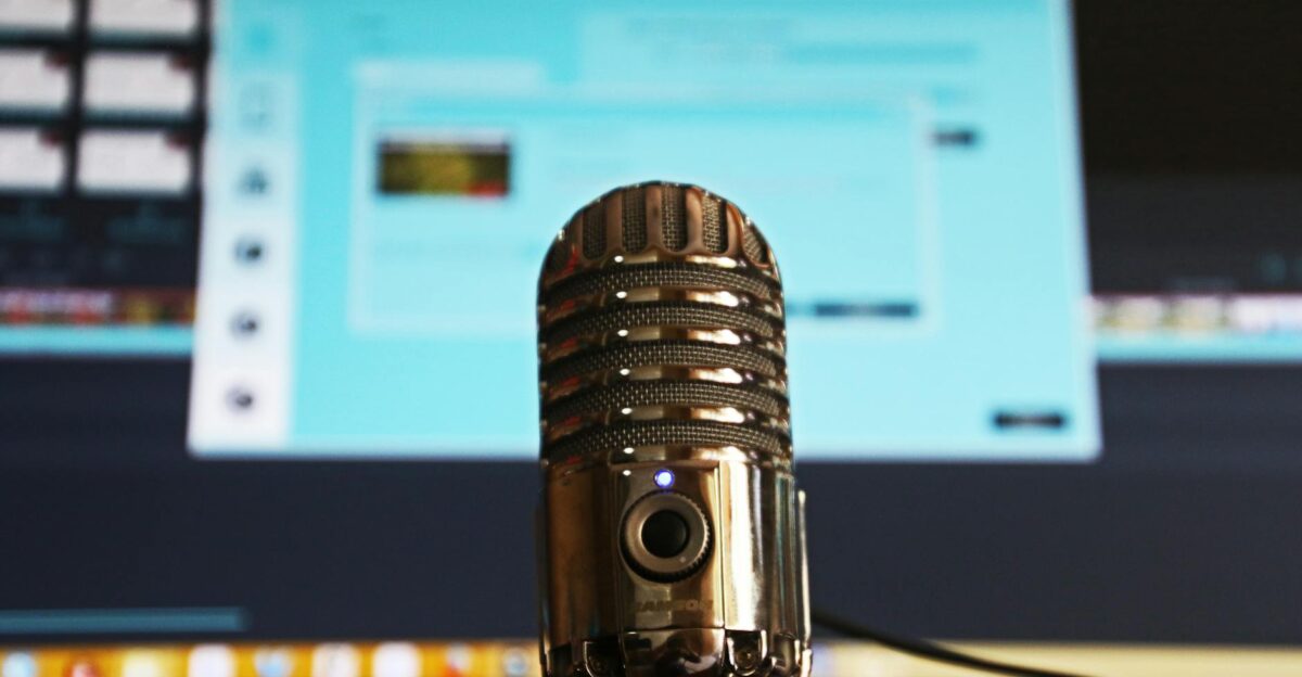 Close-up of a microphone with a blurred computer screen in the background ideal for podcast themes