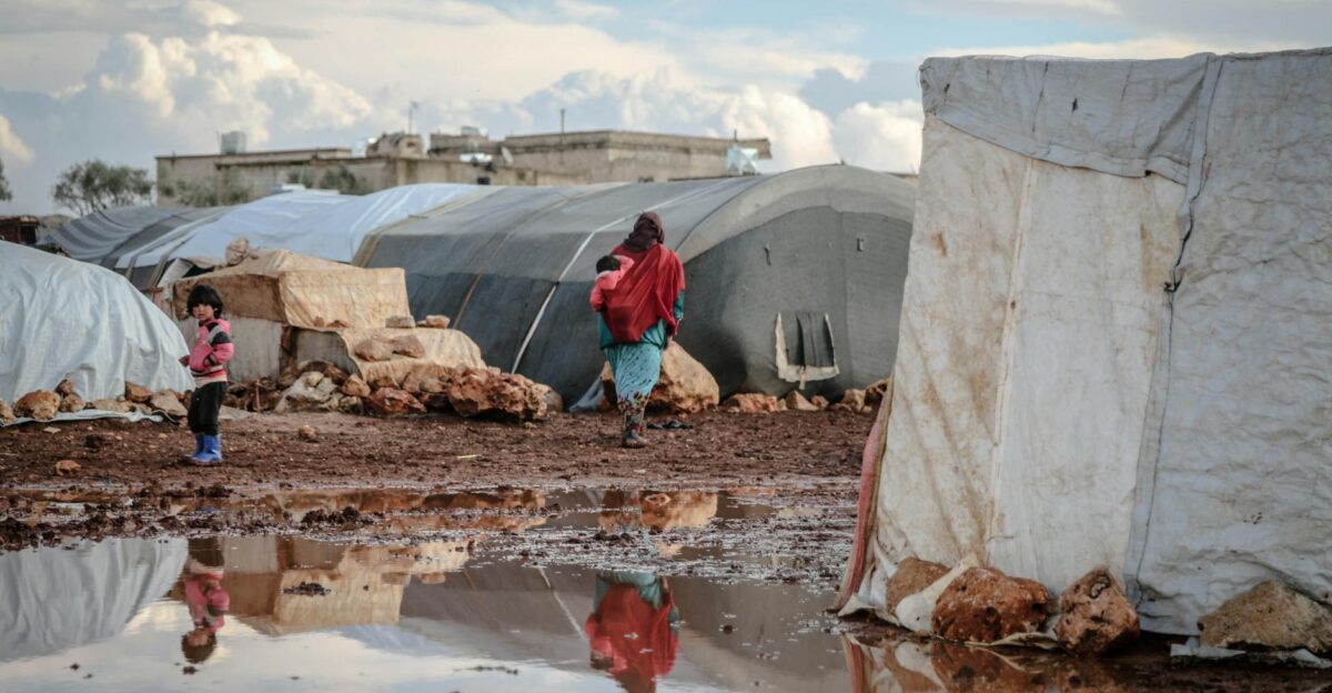A refugee camp in Idlib Syria showing tents and muddy conditions with people nearby