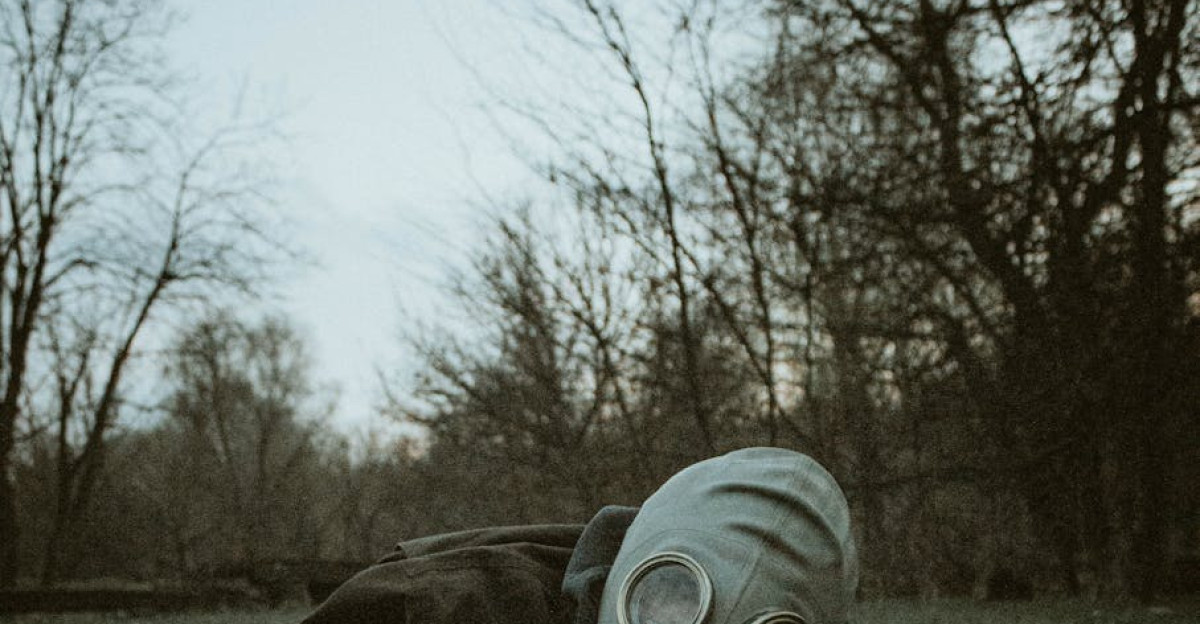 A person wearing a gas mask reaches across the grass in a moody forest setting