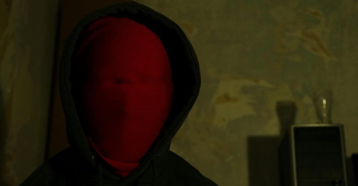 A person with a red mask and dark hoodie creating an enigmatic atmosphere indoors