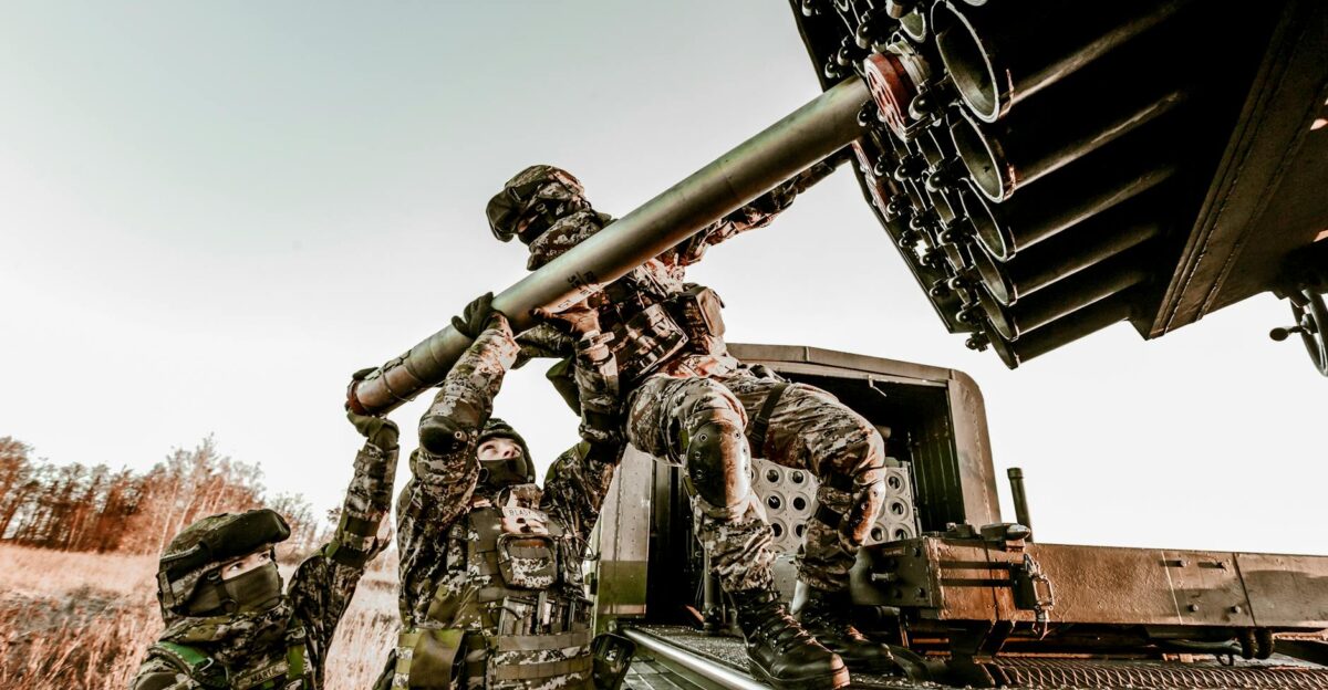 Soldiers in camouflage uniforms loading artillery equipment during a military field operation