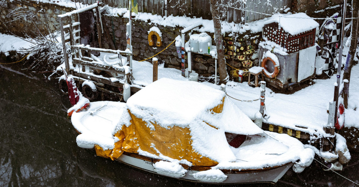 A snow-covered boat docked by a rustic fence during winter, creating a serene winter landscape.