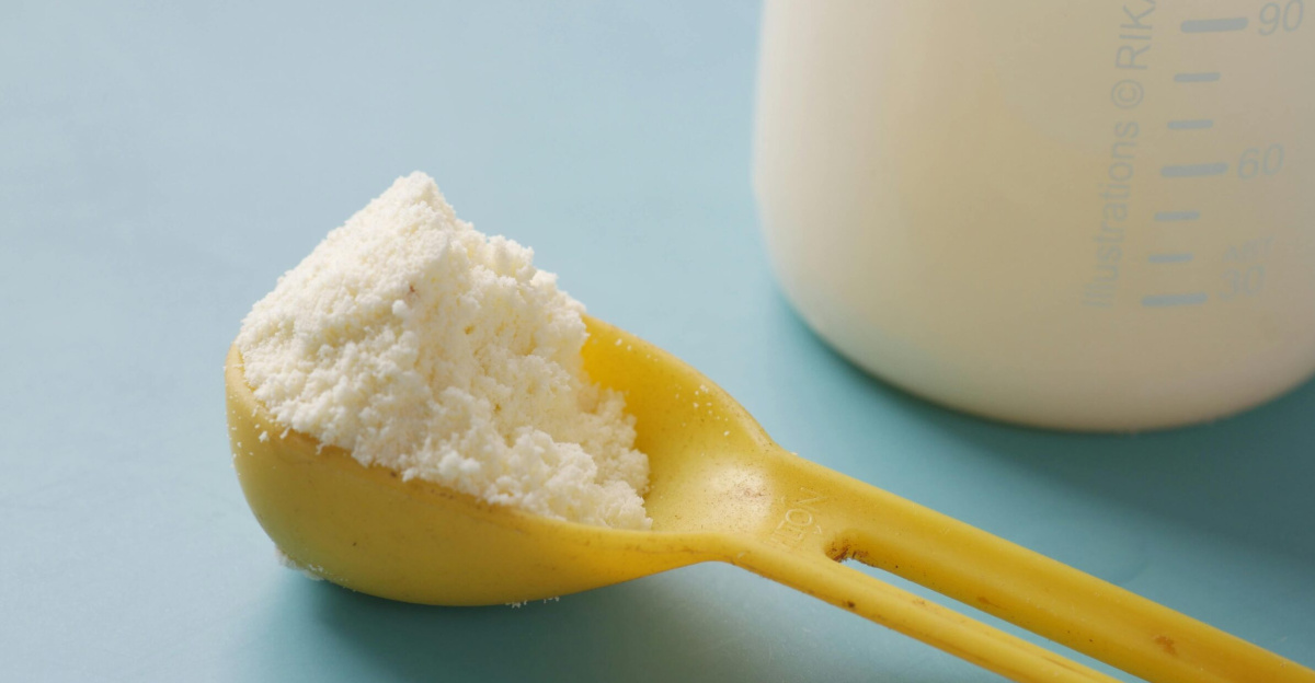 A yellow spoon filled with powdered milk, next to a measuring bottle, on a blue background.