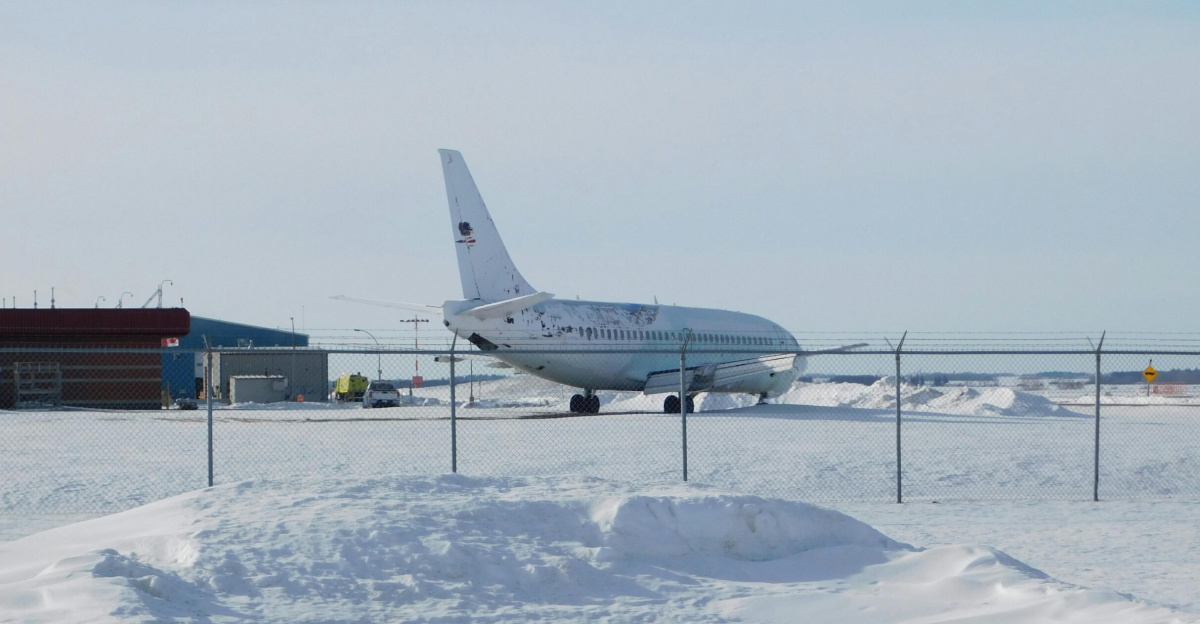 Airplane parked on a snowy runway at an airport, captured in winter conditions.