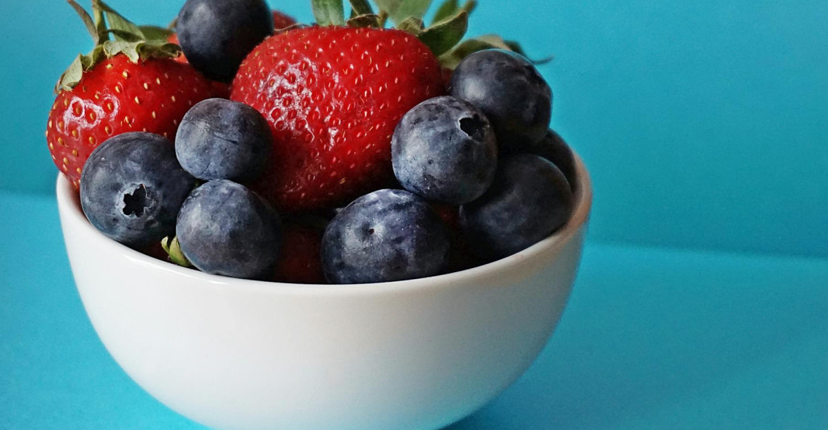 A vibrant mix of fresh strawberries and blueberries in a white bowl on a blue background