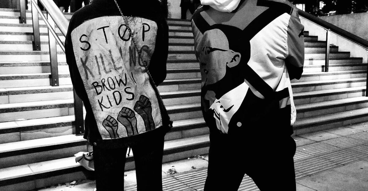 Black and white protest scene in London with activists wearing slogan jackets
