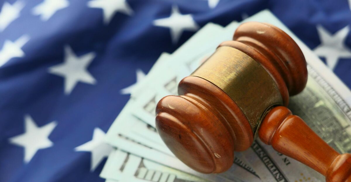 Close-up of a gavel on US dollar bills with American flag backdrop symbolizing justice and finance