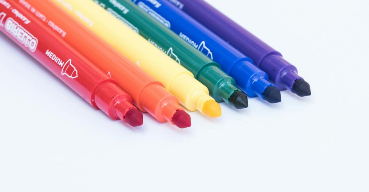 A close-up of six colorful markers arranged in a row showcasing a spectrum of rainbow colors